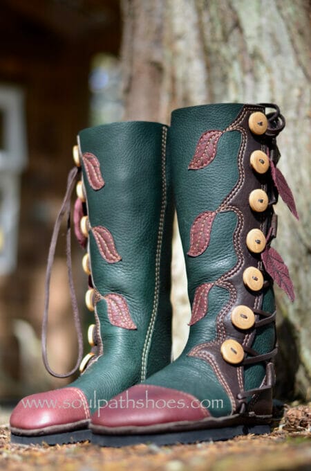 Green leather boots with brown leaf designs and tan buttons, showcased against a tree trunk backdrop. Let these boots guide your style, offering custom options to suit your unique taste.